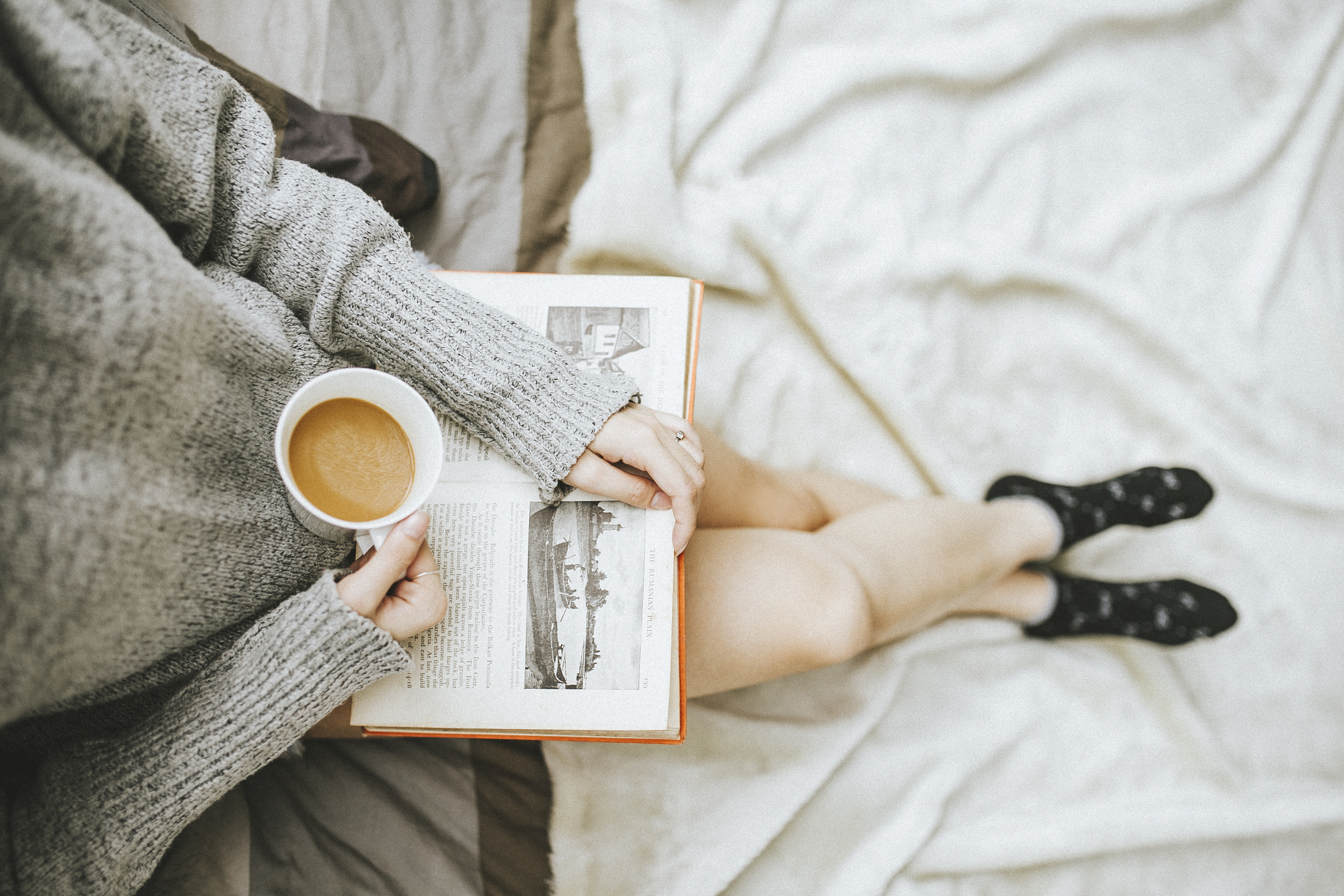 Image of a girl holding a cup of coffee with a book on her lap