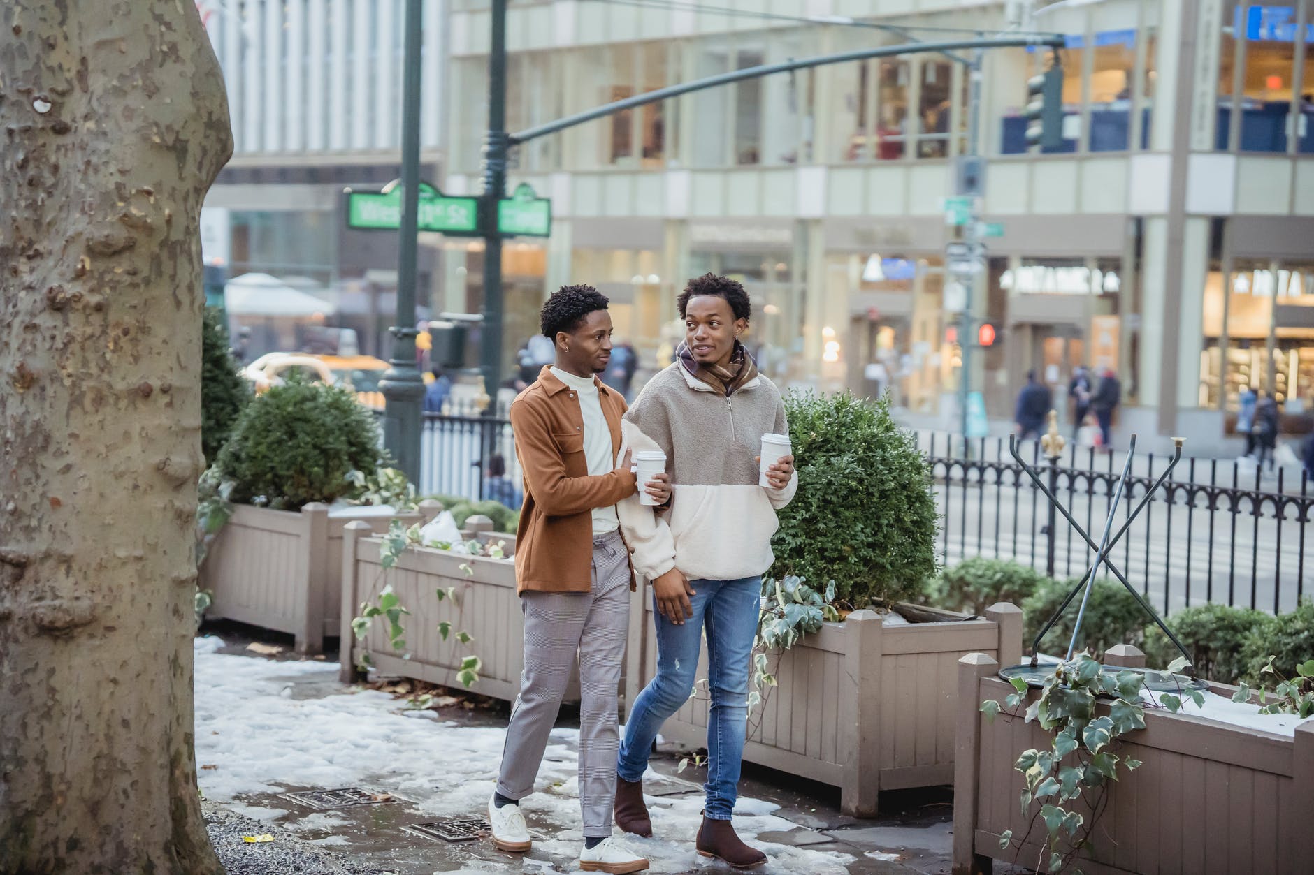 cheerful black homosexual couple with coffee walking on snowy sidewalk