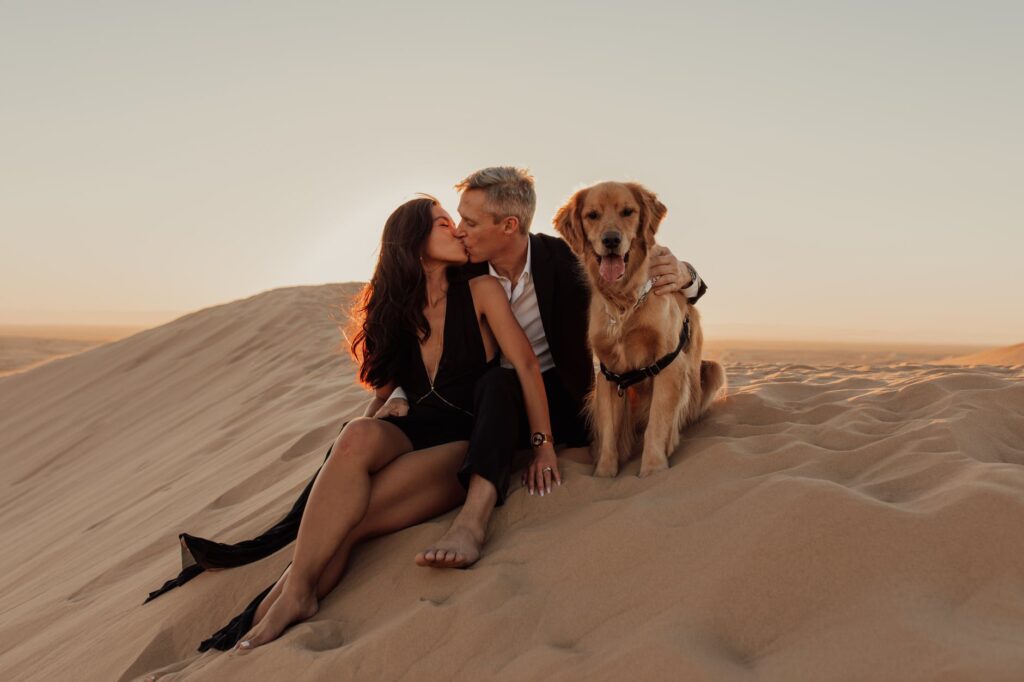 happy couple kissing while embracing fluffy dog in desert