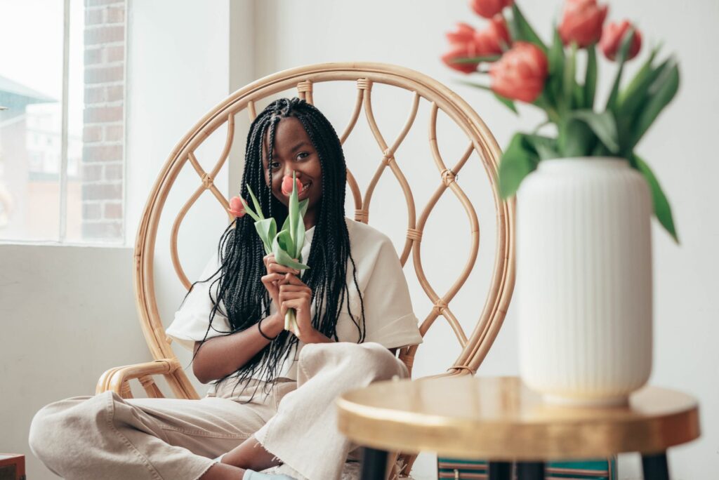 smiling young black lady smelling bunch of tulips while sitting on chair